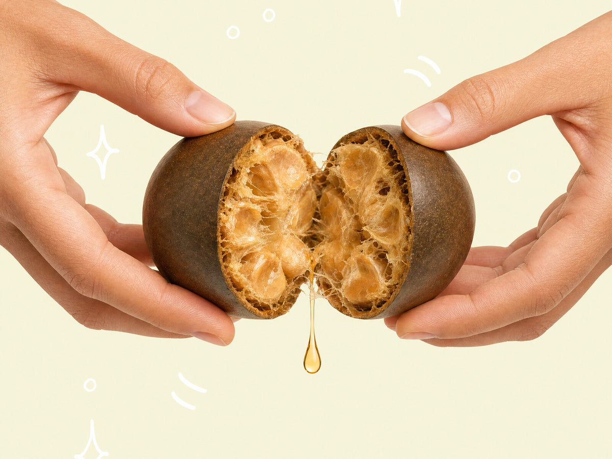 Two hands splitting a monk fruit open, a golden drop falling from the cut face